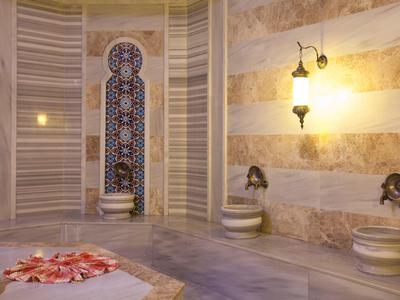 Hammam traditionnel avec murs en marbre, sièges et une mosaïque murale ornée.
