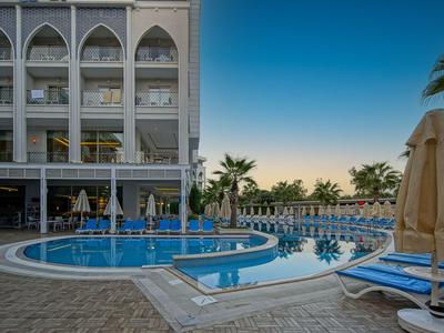 Area piscina dell'hotel con lettini e palme al tramonto.