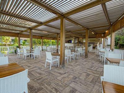 Terrasse couverte avec tables en bois et chaises blanches dans un cadre extérieur paisible.