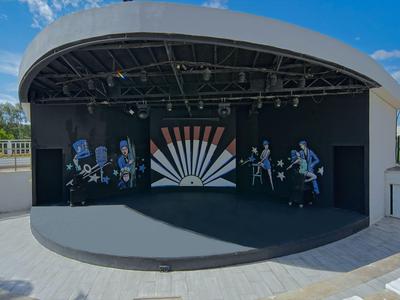 Palco all'aperto con tetto curvo e arte colorata sotto un cielo blu.