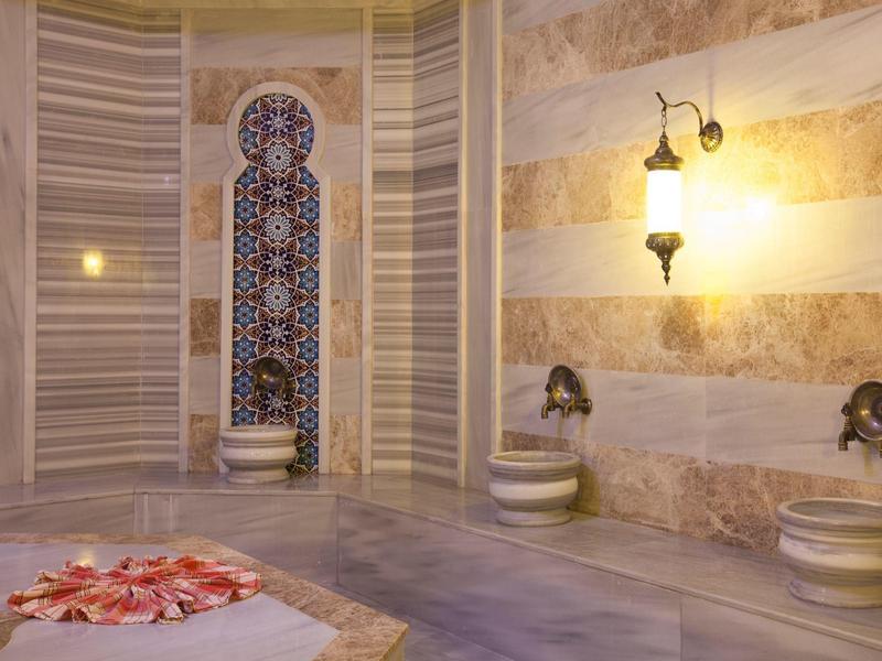 Hammam traditionnel avec murs en marbre, sièges et une mosaïque murale ornée.