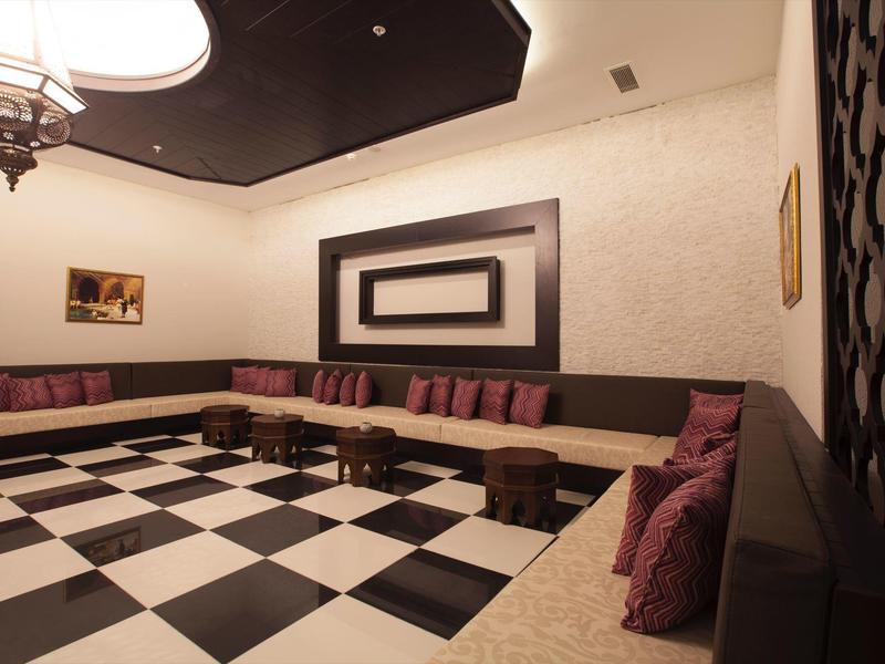 Grande pièce avec sol en damier noir et blanc, sièges bas et coussins violets.