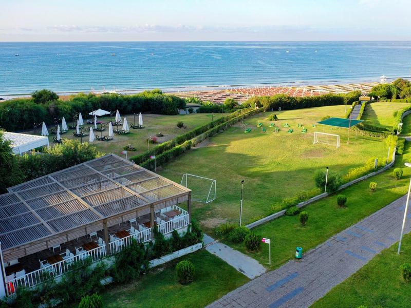 Parc de plage vert avec terrain de football, parasols et vue sur la mer bleue.