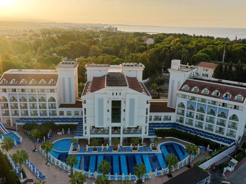 Grand hôtel avec piscine, entouré de verdure et au coucher du soleil.