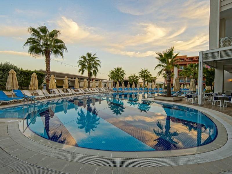Piscine ronde avec des transats bleus et des palmiers dans un complexe hôtelier au coucher du soleil.