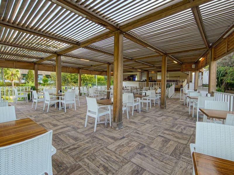 Terrasse couverte avec tables en bois et chaises blanches dans un cadre extérieur paisible.