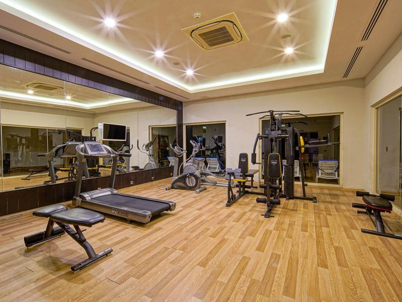 Salle de sport moderne avec bancs, tapis de course et machines de musculation devant de grands miroirs.