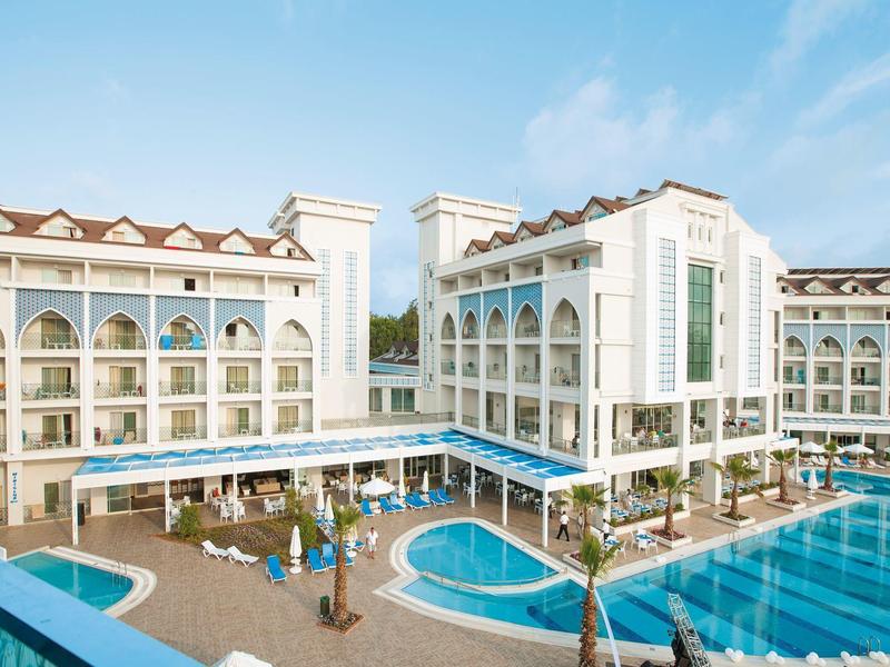 Grand hôtel avec plusieurs bâtiments autour d'une piscine et parasols bleus.