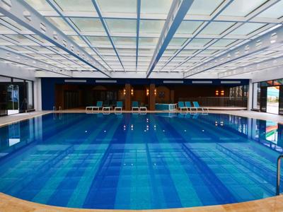 Ruim binnenzwembad met ligstoelen en glazen plafond in een modern hotel.