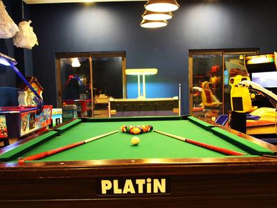 Table de billard dans une salle de jeux confortable avec diverses machines d'arcade en arrière-plan.