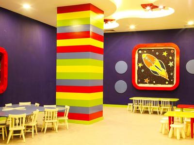 Kleurrijke speelkamer voor kinderen in een hotel met gestreepte centrale pilaar en kleine tafels en stoelen.