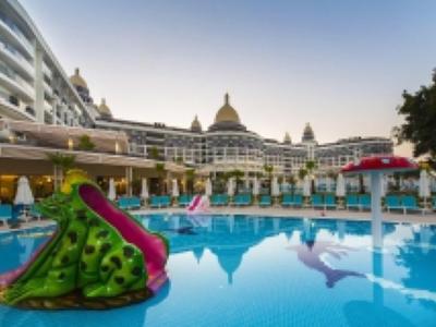 Buitenzwembad van hotel met glijbanen, omgeven door witte gebouwen en palmbomen bij zonsondergang.