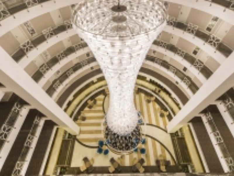 Uitzicht naar beneden op een grote, gebogen trap met een grote, sierlijke kroonluchter in het midden.