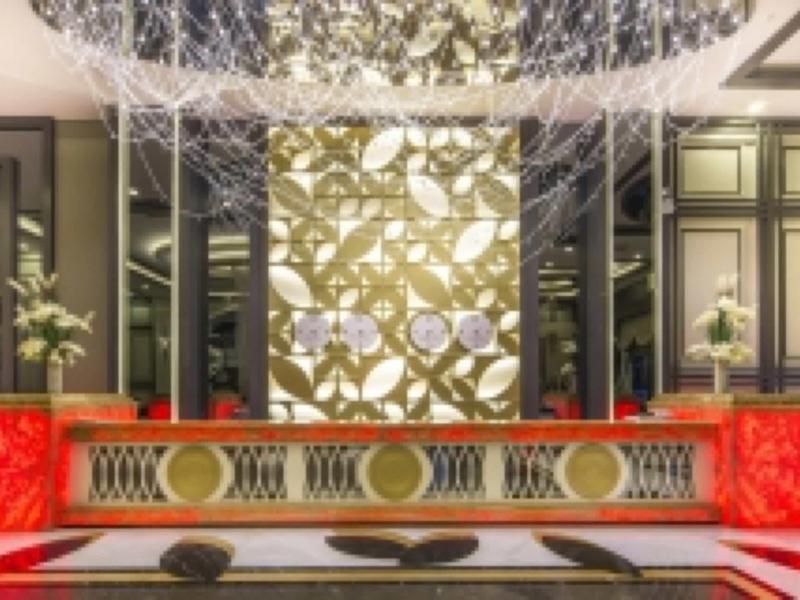 Luxe hotelreceptie met sierlijke rode balie en gouden patroon op de achtergrond.