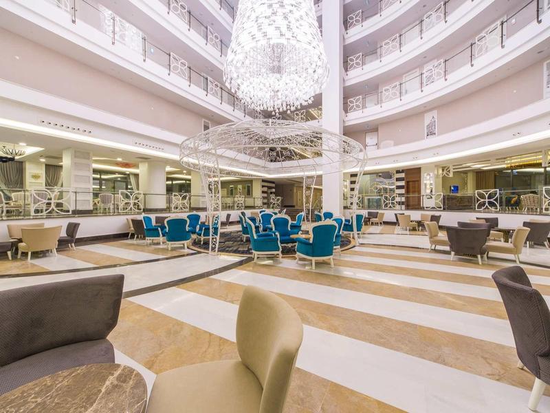 Ruime hotellobby met ronde kroonluchter, blauwe en beige stoelen en marmeren vloer.