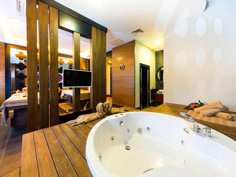 Moderne hotelkamer met houten accenten, een jacuzzi en een gezellige slaapruimte gescheiden door houten panelen.