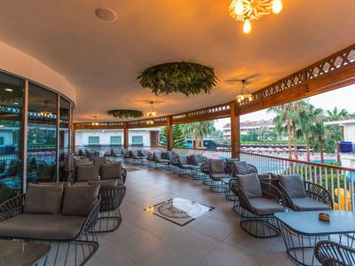Überdachte Terrasse mit vielen grauen Korbsesseln, Pflanzen und Holzgeländer mit Blick ins Freie.