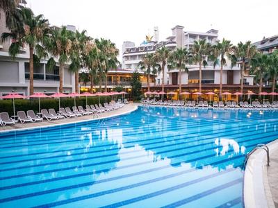 Grand piscine d'hôtel avec chaises longues et palmiers dans une station ensoleillée.
