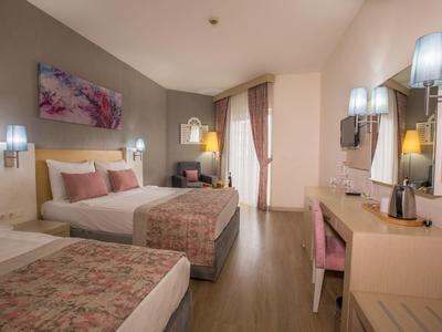 Nowoczesny pokój hotelowy z dwoma łóżkami, biurkiem i krzesłem, jasne drewniane meble i ciepłe oświetlenie.