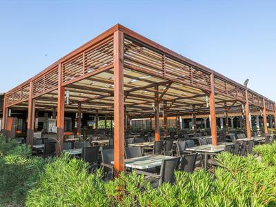 Restaurante al aire libre con estructura de madera y metal, mesas y sillas de madera bajo cielo despejado.
