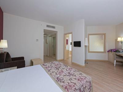 Jasny pokój hotelowy z podwójnym łóżkiem, sofą, biurkiem i dużym lustrem.