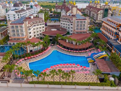 Grande piscina blu dell'hotel circondata da palme e ombrelloni rosa tra edifici a più piani.