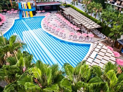 Gran piscina de hotel con toboganes, sombrillas rosadas y palmeras verdes.