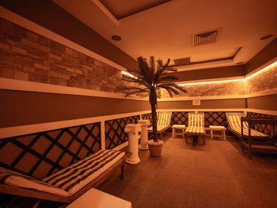 Accogliente area lounge dell'hotel con posti a sedere, tavolo e palma decorativa sotto luce calda.