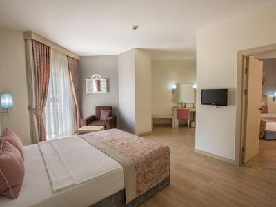 Camera d'hotel luminosa con letto matrimoniale, poltrona, scrivania e camera adiacente.