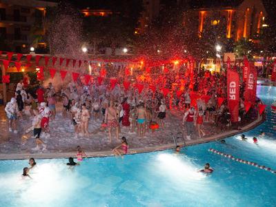 Des personnes fêtent et nagent lors d'une fête nocturne à la piscine avec éclairage rouge.