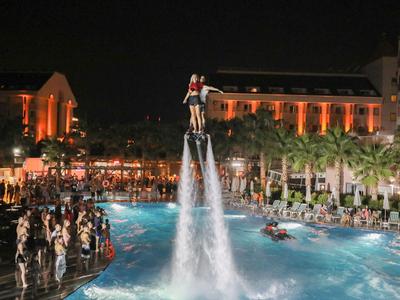 Personne vole avec un jetpack aquatique au-dessus d'une piscine d'hôtel éclairée la nuit devant un large public.