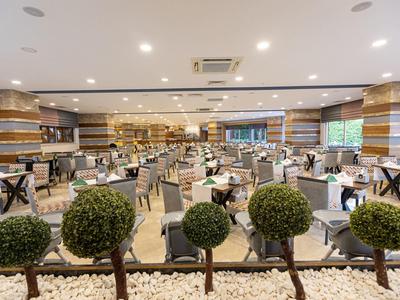 Duża, nowoczesna sala jadalna w hotelu z wieloma stołami i dekoracyjnymi roślinami.