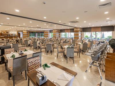 Duża, nowoczesna, dobrze oświetlona jadalnia z elegancko nakrytymi stołami i szarymi krzesłami.