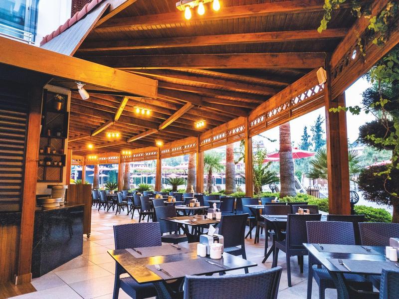 Zadaszony taras restauracyjny z drewnianym sufitem i nakrytymi stołami.