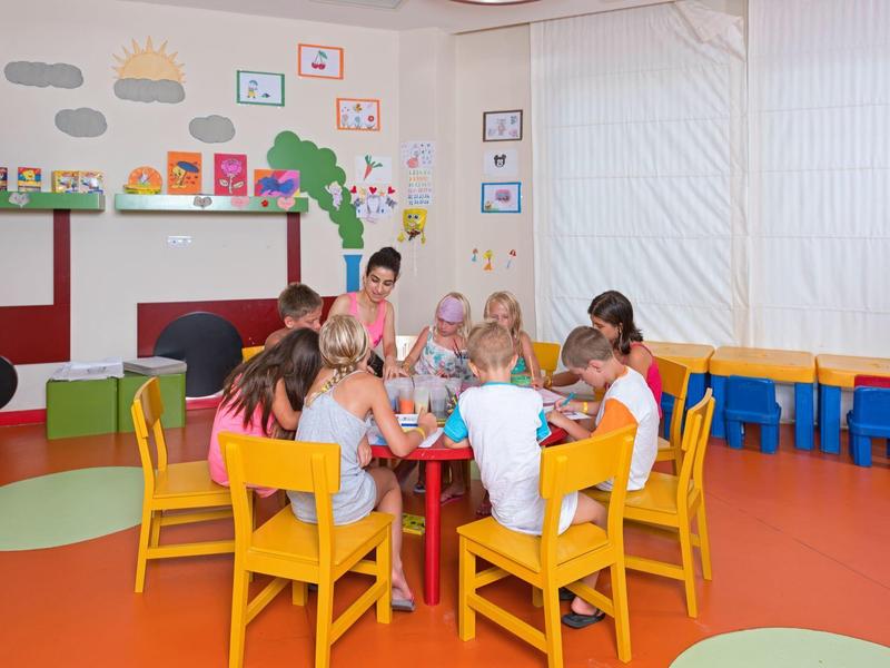 Dzieci siedzą przy stole na żółtych krzesłach w kolorowym, zabawnym pokoju.