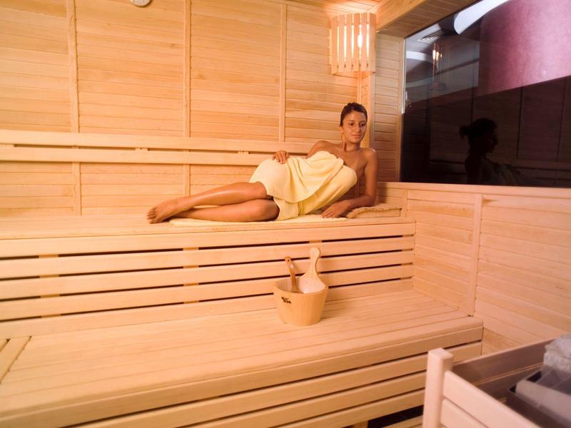 Kobieta w żółtym ręczniku relaksuje się w jasnej drewnianej saunie bio z dzbankiem wody.