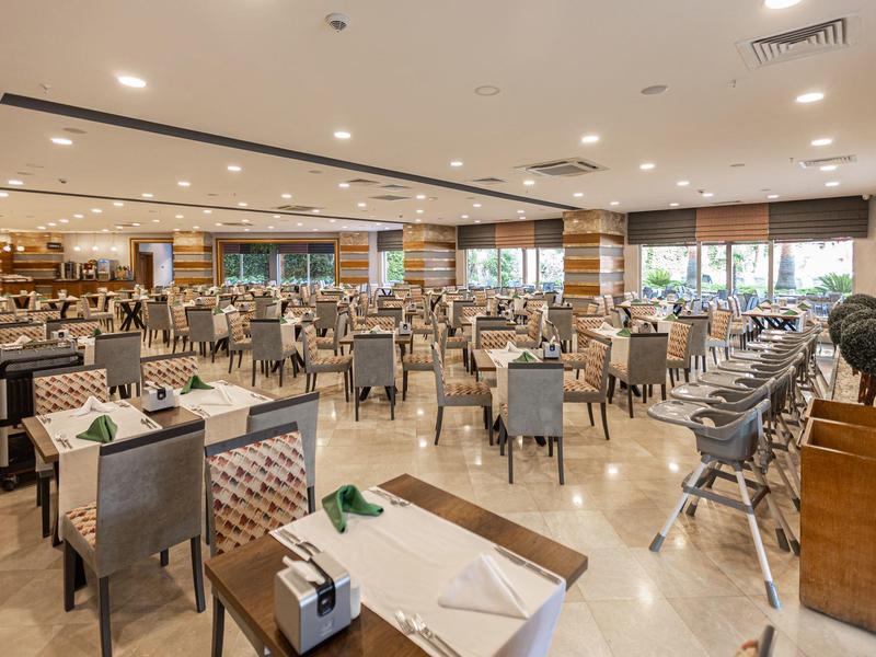 Duża, nowoczesna, dobrze oświetlona jadalnia z elegancko nakrytymi stołami i szarymi krzesłami.