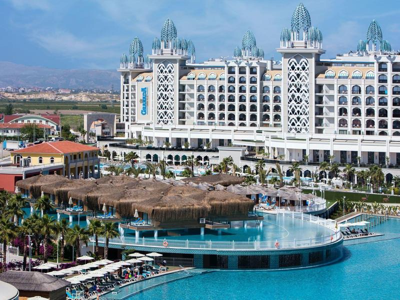 Luksusowy biały hotel z okrągłym basenem i parasolami w tropikalnym otoczeniu.