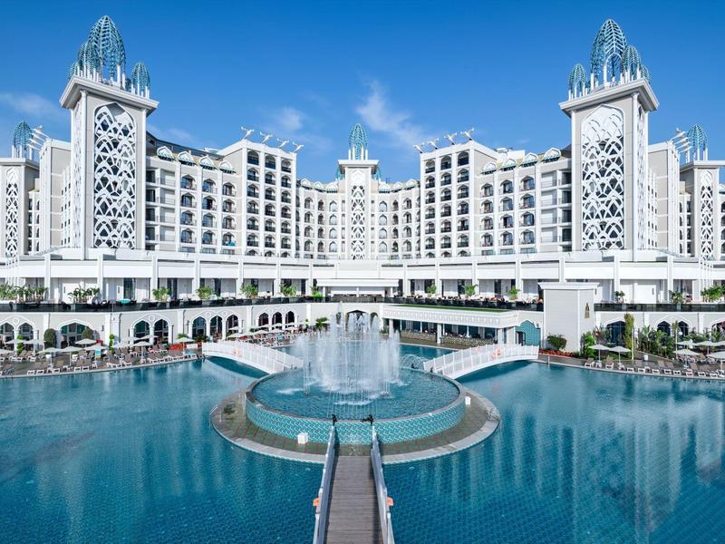 Duży luksusowy hotel z basenem i fontanną pod jasnym niebem.