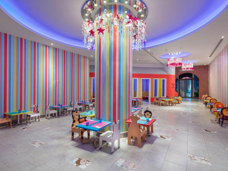 Kolorowa sala zabaw dla dzieci z stołami, krzesłami i jasnymi dekoracjami.