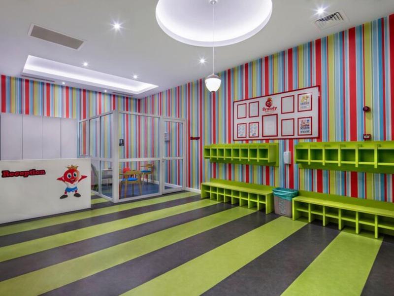 Kolorowy pokój zabaw z paskowanymi ścianami, zielonymi półkami i bezpiecznym placem zabaw.