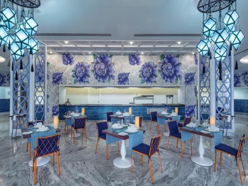 Nowoczesna sala restauracyjna z okrągłymi stołami i eleganckimi niebieskimi krzesłami.