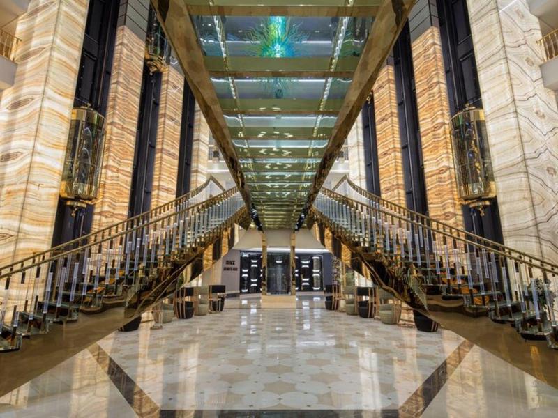 Hol hotelowy z dużymi schodami centralnymi, błyszczącą marmurową podłogą i eleganckim wystrojem.