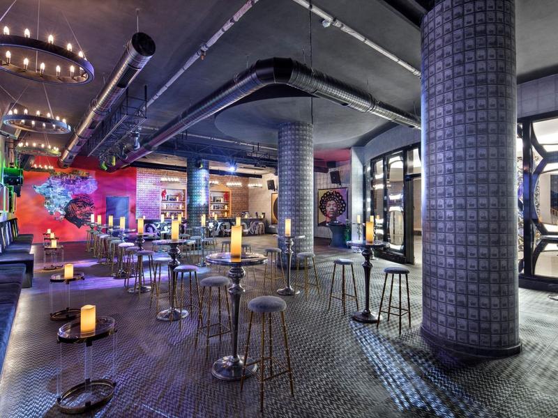 Nowoczesny bar z nastrojowym oświetleniem, kolorowymi ścianami i przemysłowymi meblami.