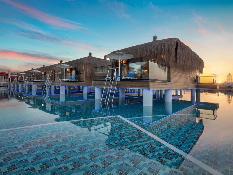 Bungalowy na palach nad wodą z basenem o zachodzie słońca.