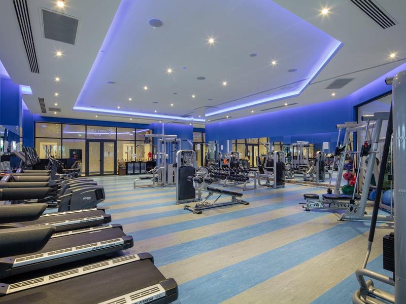 Nowoczesna siłownia z różnorodnym sprzętem i kojącym niebieskim oświetleniem.