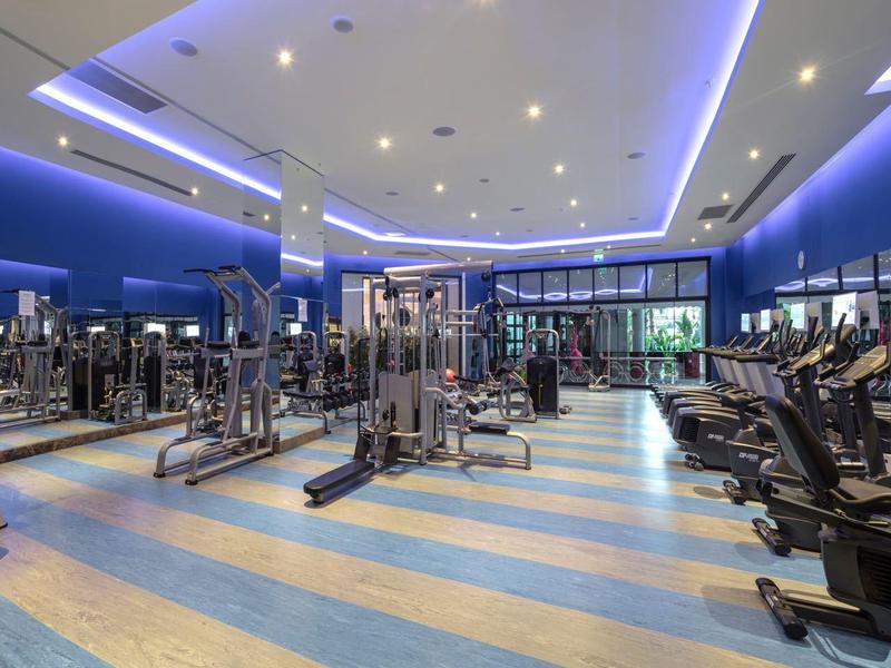 Nowoczesna siłownia z różnorodnym sprzętem i intensywnym niebieskim oświetleniem.