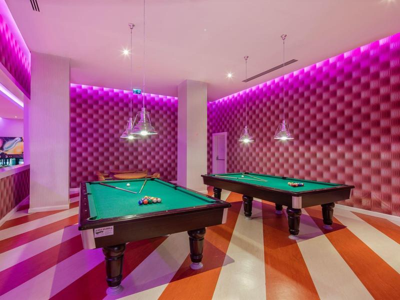 Sala gier z dwoma stołami bilardowymi i fioletowym oświetleniem.
