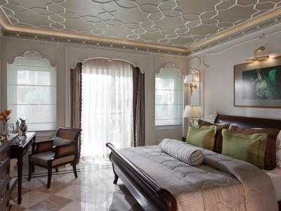 Elegantes Schlafzimmer mit Doppelbett, Schreibtisch, Stühlen und großen Fenstern mit Vorhängen.