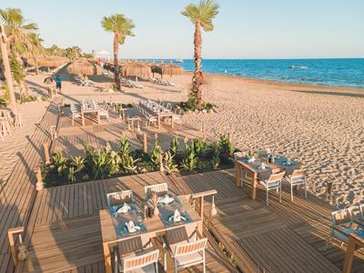 Strandrestaurant mit Holzboden, gedeckten Tischen und Palmen am Meer bei Sonnenuntergang.